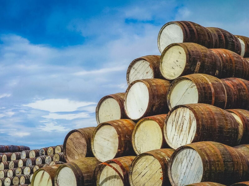 Stacked oak whiskey barrels outside a traditional Scottish distillery.