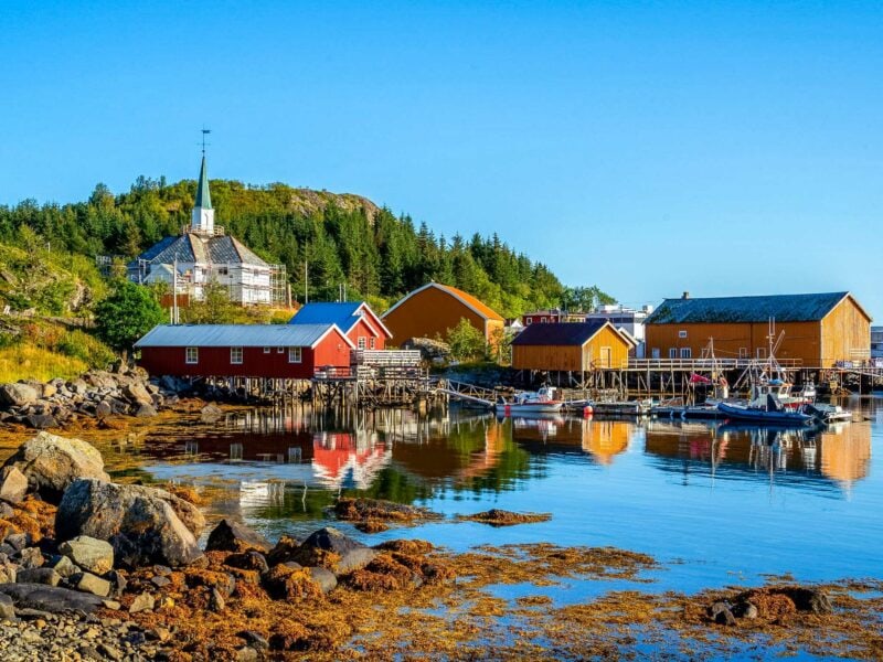 Brightly painted red and yellow houses with boats moored along the rocky shoreline of a small fishing village.