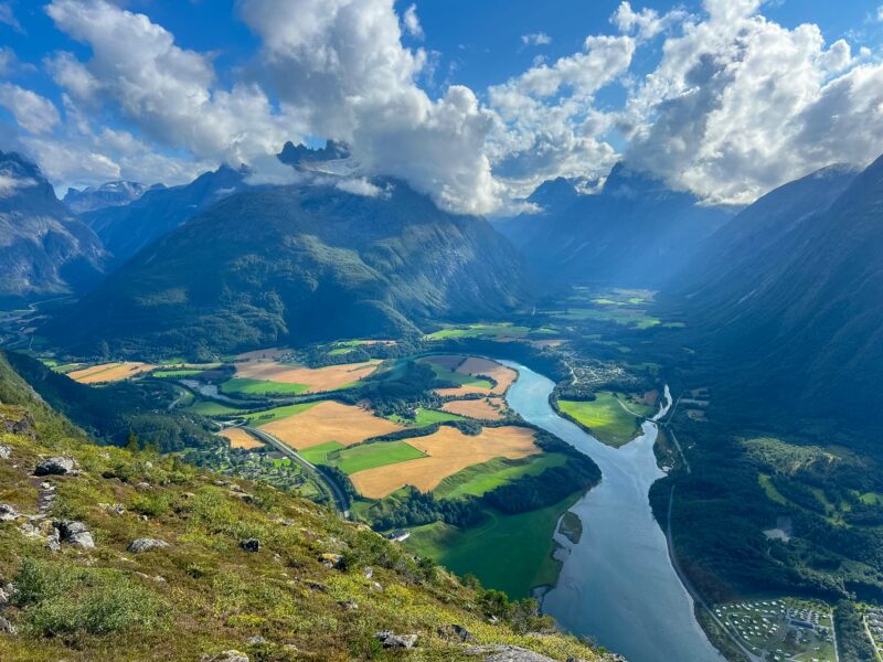 Expansive aerial view from top of cable car Andalsnes, of valley with winding river, patchwork fields, and towering mountains under dramatic clouds