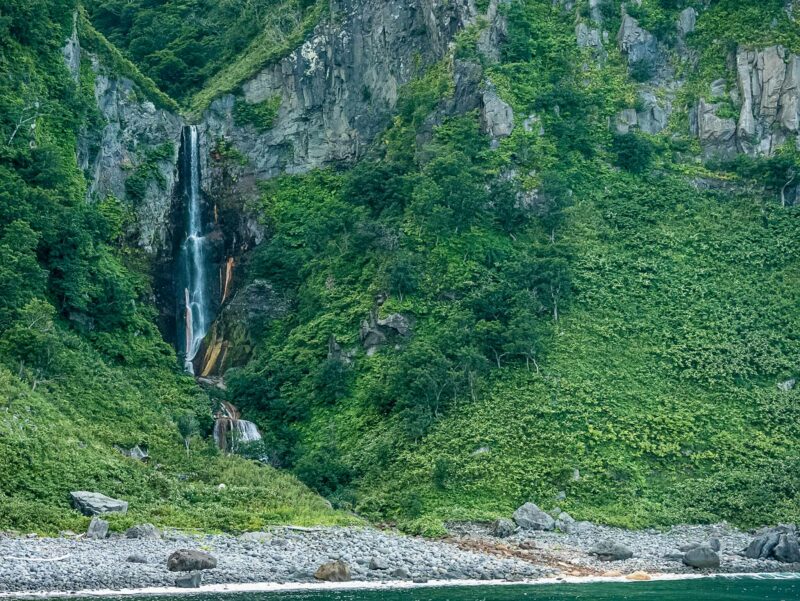 Dramatic waterfall plunging down a sheer greened cliff face into a rocky basin.