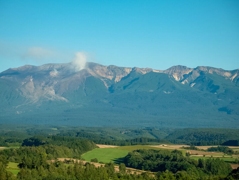 Broad volcanic peak rising above patchwork farmland and forest under a clear sky.