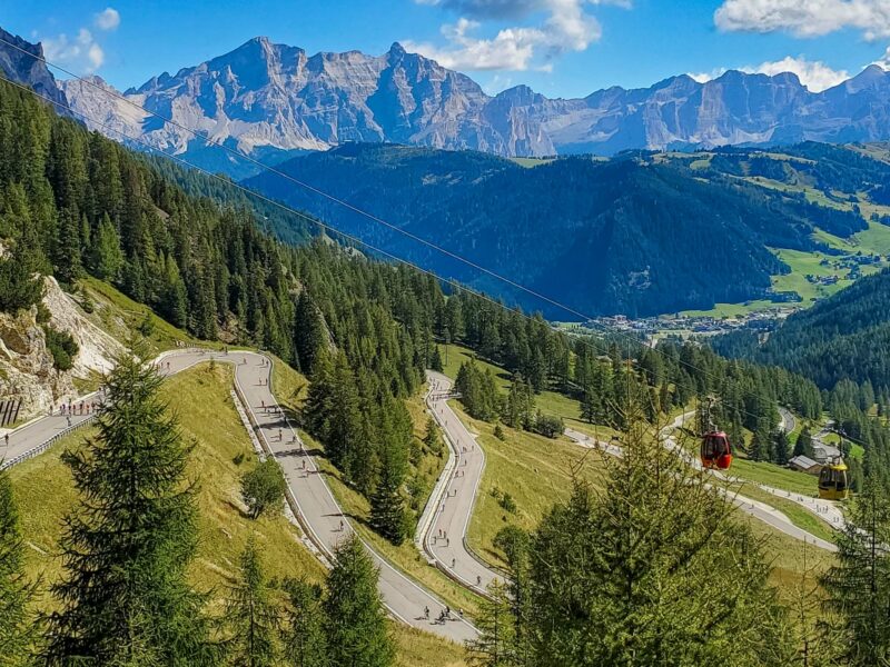 Winding road through the Dolomites with cyclists and cable cars
