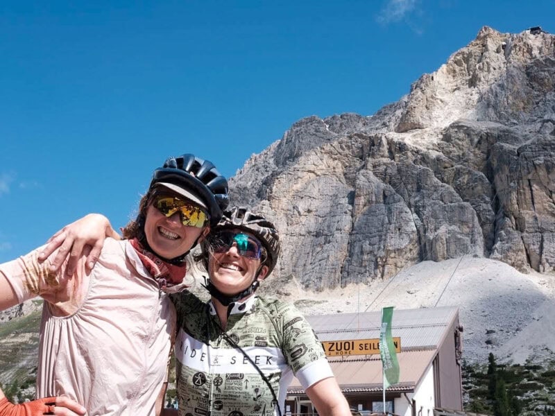 Two cyclists smiling before rocky mountain backdrop