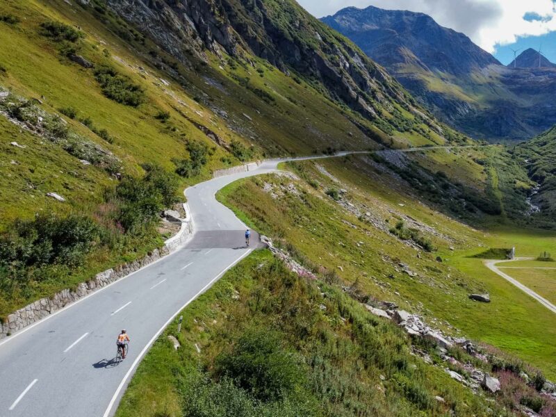 Cyclists riding winding mountain road through green valley