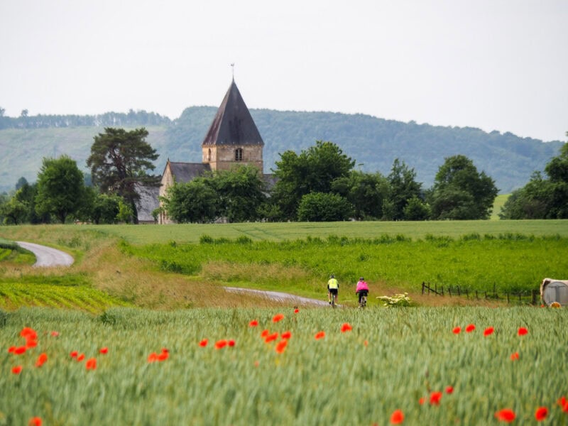 Cyclists riding past country church and poppy field
