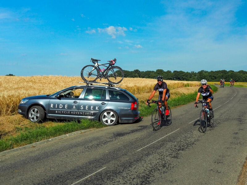 Cyclists riding beside support car in rural countryside