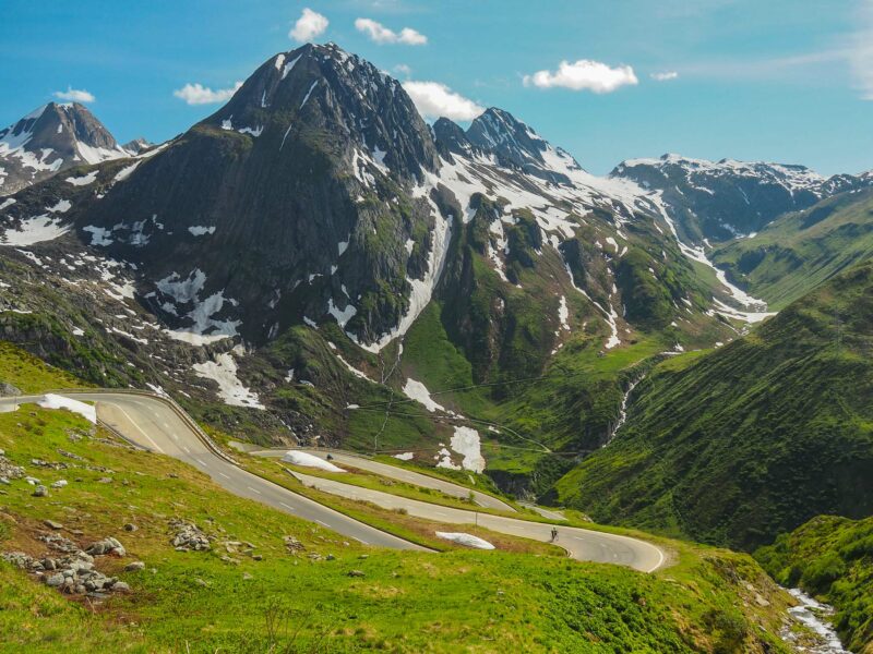 Winding mountain road through green valley and snowy peaks