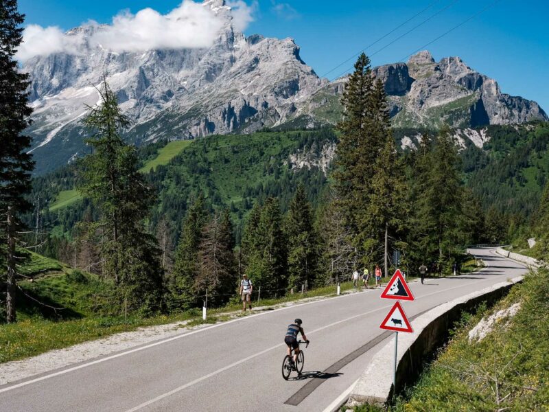 Cyclist on alpine road beneath rugged mountains