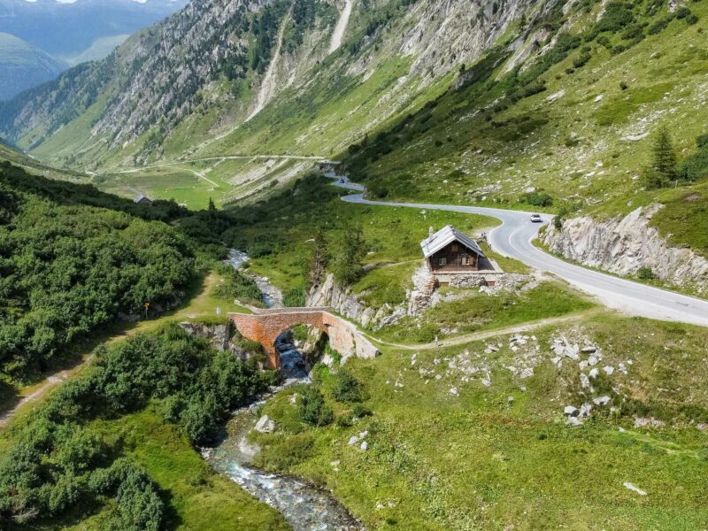Winding alpine road beside cabin and stone bridge