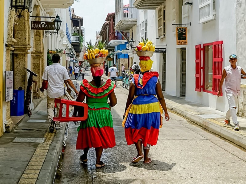 Palenqueras in traditional dress carrying fruit baskets through the colonial streets of Cartagena, Colombia, on the Bolivar cycling tour