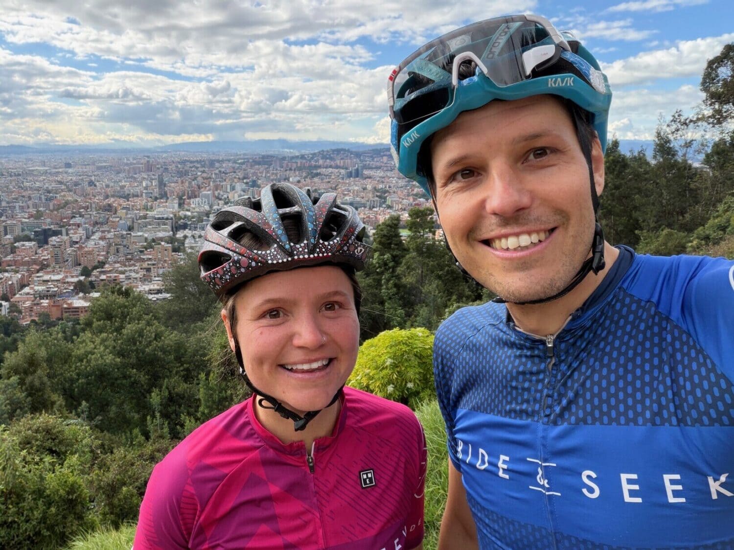 Ben and Beatrice from Ride & Seek cycling above Bogotá, Colombia, with the city skyline in the background