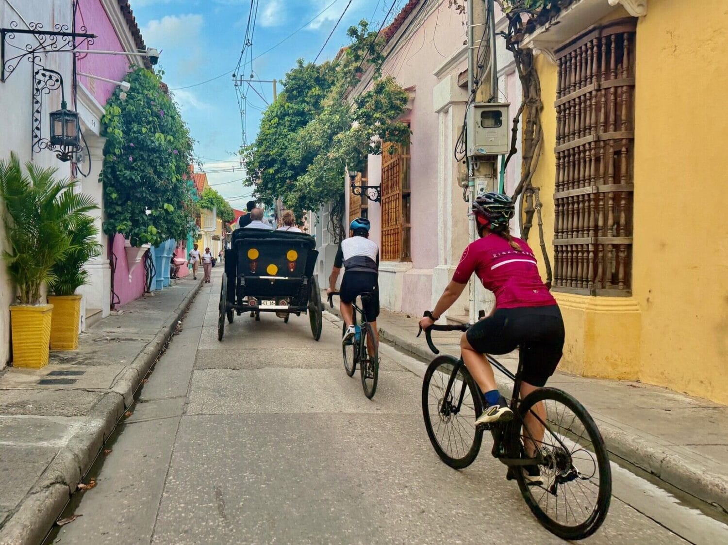 Cyclists riding past a horse-drawn carriage through the colourful colonial streets of Cartagena, Colombia