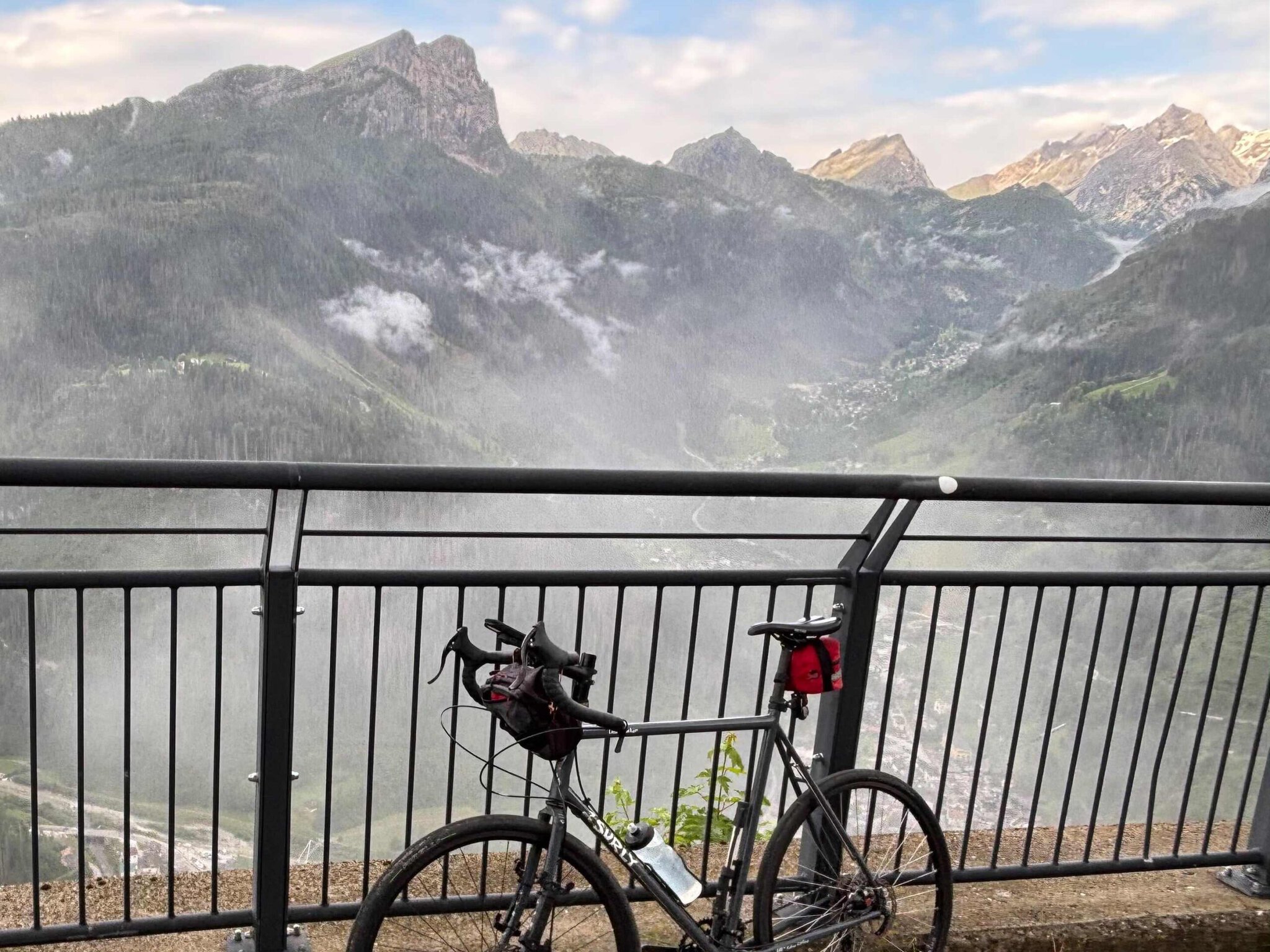 Paul's Surly touring bike parked against a railing overlooking misty mountain peaks at Colle San Lucaia on the Caesar Tour