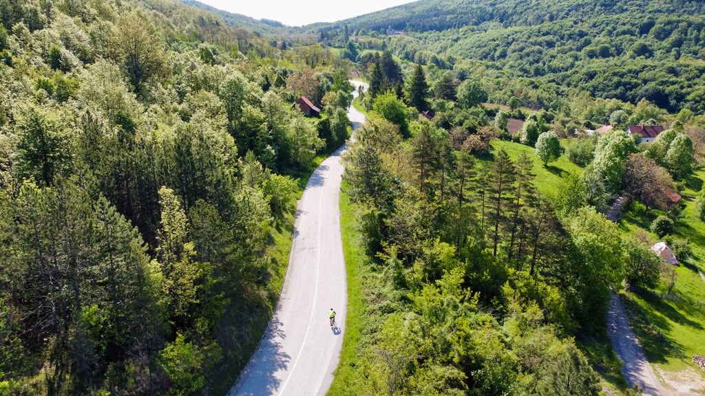 Aerial view of Paul riding along a winding paved road surrounded by dense green forest on the Ride and Seek Sultan's Trail