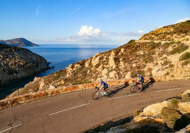 3 Islands Corsica 8300 2 cyclists riding on a cliff edge road along the coast of Corsica overlooking the ocean