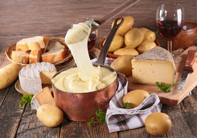 Aligot A spoon that has been dipped in melting aligot which is now is oozing back into the pot below. Surrounding this is an array of breads.