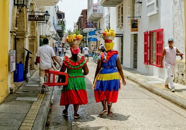 Palenqueras in traditional dress carrying fruit baskets through the colonial streets of Cartagena, Colombia, on the Bolivar cycling tour