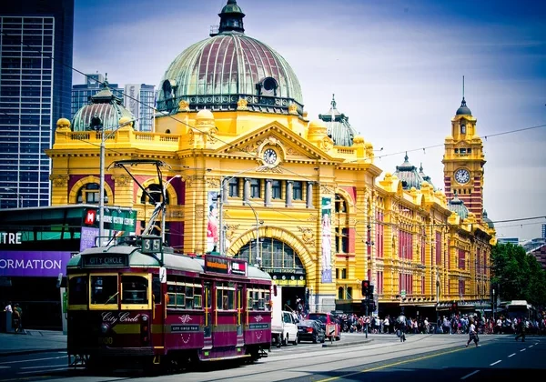 A large heritage train station is the background to a traditional Melbourne tram.