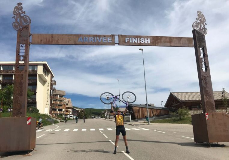 A cyclist holding his bike above his head at the Alpe d'Huez finish line