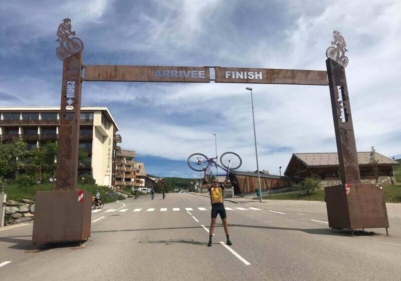 Paul holding his bike above his head at the Alpe d'Huez finish line