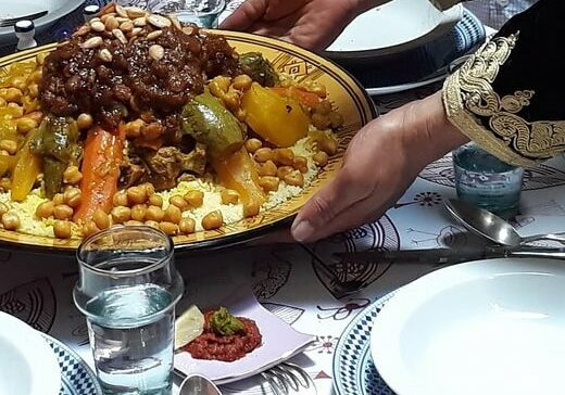 Reconquista Darori Resto Fes Morocco A large Moroccan couscous dish served with chickpeas, carrots, zucchini, peppers, and lamb, topped with caramelized onions and almonds, presented on a decorated platter.