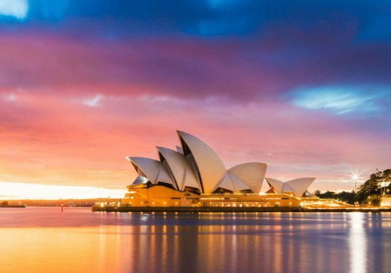 Sydney Opera House The Sydney Opera House is photographed from across the Harbour, with a colourful cloudy sky in the background.